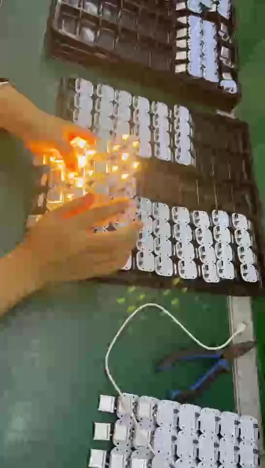 A tray of assembled boards held in gloved hands, with the LEDs on the boards lit, on a workbench.