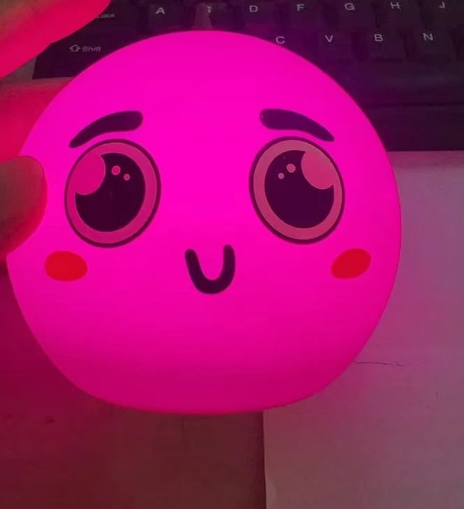 The indoor ambient light held in one hand, with the printed face on the silicone body lit up in pink.